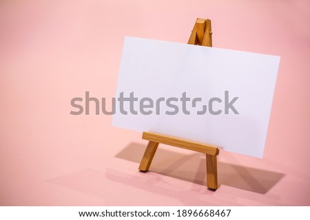 Wooden easel with white sheet. Pink background.