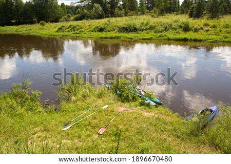 River in summer on a sunny day, green grass and forest. Reflection in the water. Domestic tourism, ecotourism, unity with nature. Clean environment, protection. Water hiking and camping. Summertime.