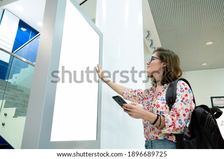 Woman with phone uses self-service desk with touch screen Royalty-Free Stock Photo #1896689725