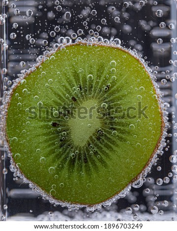 Macro shot of kiwi slice in a glass with sparkling water on black background.