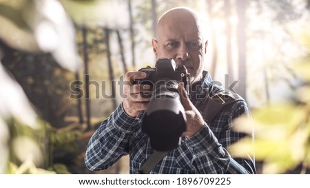 Professional photographer shooting in a forest, he is looking at camera