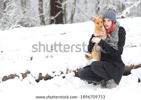 Attractive red hair girl is holding her brown dog in her arms in wintry snovy nature.