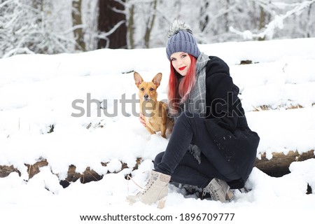 Smiling attractive red hair girl is posing with her brown dog in wintry snovy nature.