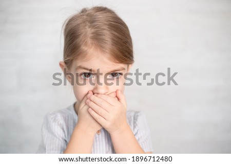 portrait of little girl, child closing his mouth with hands. Speech therapist, speech problems, stammering, mumbling. Royalty-Free Stock Photo #1896712480