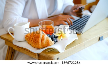 Breakfast in a tray on the bed in the luxury hotel room in front of an Asian businesswoman traveler work with a laptop, healthy food concept.