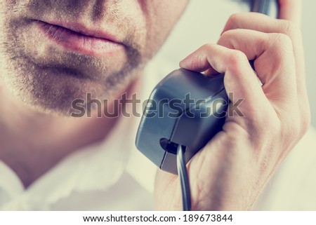 Close up of the mouth and chin of an unshaven man listening to a telephone conversation holding the receiver in his hand , vintage style instagram effect.