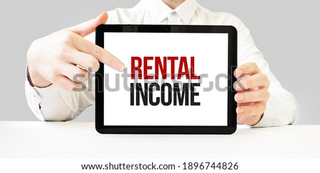 Text RENTAL INCOME on tablet display in businessman hands on the white bakcground. Business concept