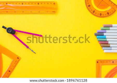 Overhead image of ruler, triangles, protractor, compass and markers on yellow background with copy space in the middle.