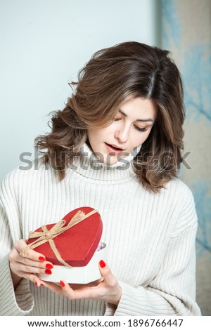 Beautiful girl open red heart gift box. Valentine's day. Happy Birthday.  Girl receives a gift at home. Womens Day message. March 8