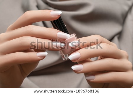 Female hands with white nail design. White glitter nail polish manicure. Woman hands on grey fabric background Royalty-Free Stock Photo #1896768136