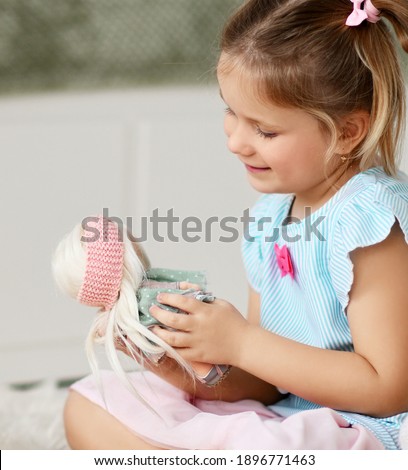 Portrait profile of cute kid girl in home dress sitting on soft carpet at home playing talking with her favorite doll. Happy childhood, cheerful lifestyle, games, comfortable pastime, hobby concept