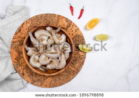 Raw shrimps or prawns in wooden plate with lime and red hot pepper ready for cooking. A bowl of fresh raw pacific white shrimp, ingredients for cooking, seafood. Top view, space for text
