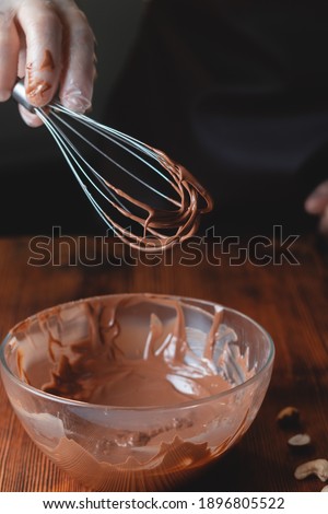 Picture of whisk with chocolate for cake preparation, sweet cake glaze home made process with cocoa melt together to create a glaze for sweet cake and chocolate, close up