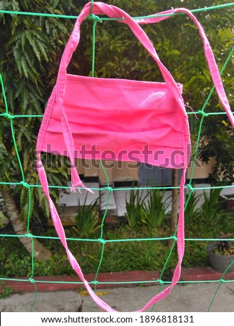 Reusable cloth face mask is hanging on a net, being dried in the sun