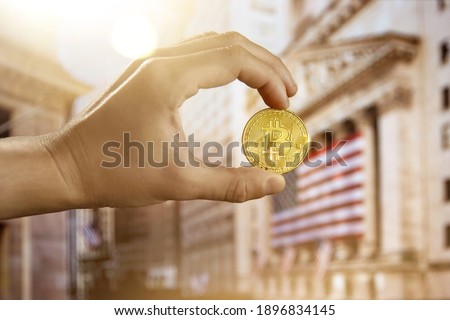 Bitcoin coin being held up outside the New York City Stock exchange building.