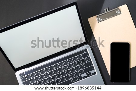 Cropped shot of Workspace laptop blank screen with smartphone on file with black background.