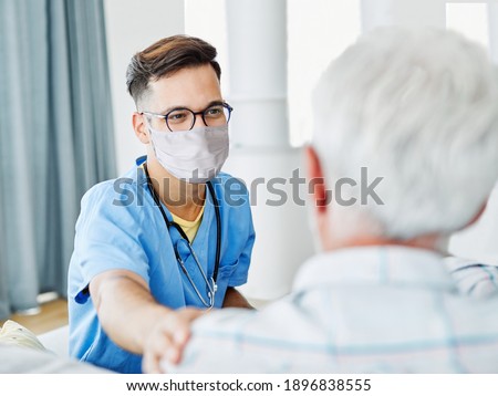 Doctor or male caregiver with senior man wearing protective mask at home or nursing home