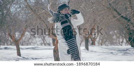 Beautiful young woman is putting her black scarf in a cold day surrounded by snowy nature. Winter Forest Landscape Background. Snow Concept 2021. 