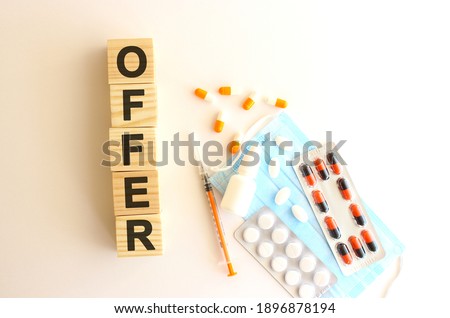 The word OFFER is made of wooden cubes on a white background with medical drugs and medical mask.