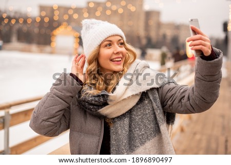 The girl is filming her video blog at the New Year's fair. In the background we see a skating rink