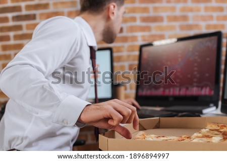 Businessman taking tasty pizza in box near computers on blurred background in office