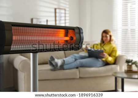 Woman reading book in living room, focus on electric infrared heater Royalty-Free Stock Photo #1896916339