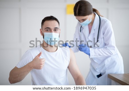 Get vaccinated. Young Caucasian guy showing thumbs up during coronavirus vaccination at clinic, promoting covid-19 immunization. Protection against global virus concept Royalty-Free Stock Photo #1896947035