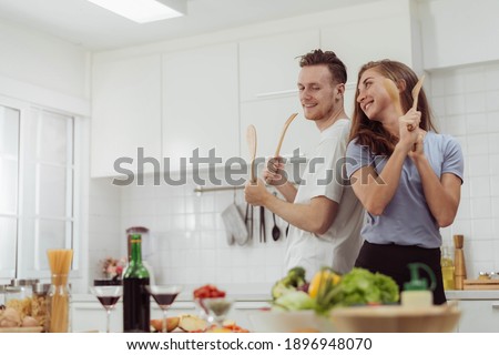 Young Beautiful couple love is dancing while cooking together in the kitchen. Happy loving man and woman cooking healthy food at home. Royalty-Free Stock Photo #1896948070