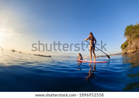 Active paddle boarder at sunset sea. Young mother with little clild paddling on stand up paddleboard. Healthy lifestyle. Water sport, SUP surfing tour in adventure camp on family summer beach vacation Royalty-Free Stock Photo #1896952558