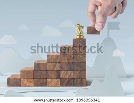 Business growth, business success or career path success concept. A knight chess is on the top of wooden stacked staircase in paper cut scene background with a hand is putting the next wooden piece.