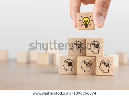 Brainstorming, creative idea or innovative idea concept. Wooden blocks with gear head icon arranged in pyramid stair shape and a man is holding the top one with light bulb icon. Royalty-Free Stock Photo #1896956374