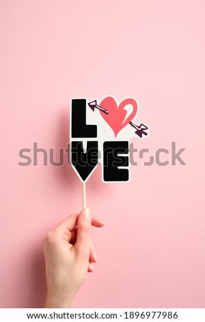 Woman's hand holding Valentines day decoration with sign LOVE over pink background. Top view.