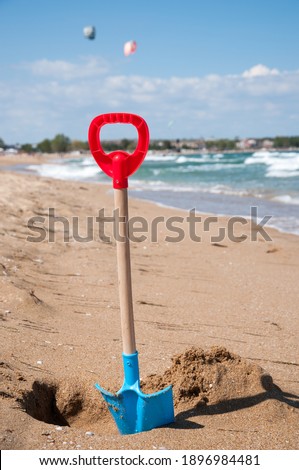 Children's blue and red shovel, hammered into the sand on the beach