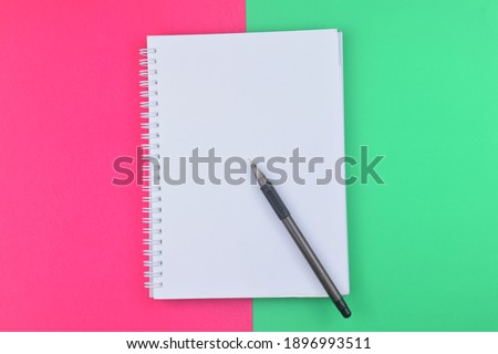 A blank notebook with pen on green and pink background . Business and education concept.