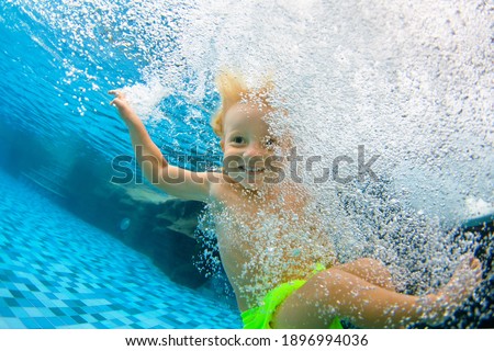 Funny portrait of child learning swimming, dive in blue pool with fun - jumping deep down underwater with splashes. Healthy family lifestyle, kids water sports activity, swimming lesson with parents.