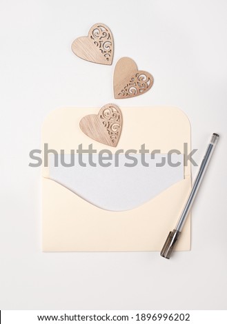 Envelope with a blank sheet of paper inside and wooden hearts on the white background. Romantic love letter for the Valentine's day concept. Space for text.