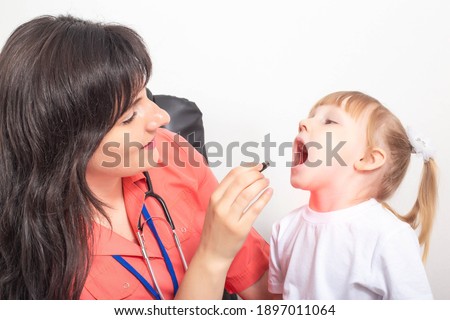 Doctor pediatrician examines the throat of a little girl who has a sore throat. Sore throat treatment concept caused by infection and tonsillitis Royalty-Free Stock Photo #1897011064
