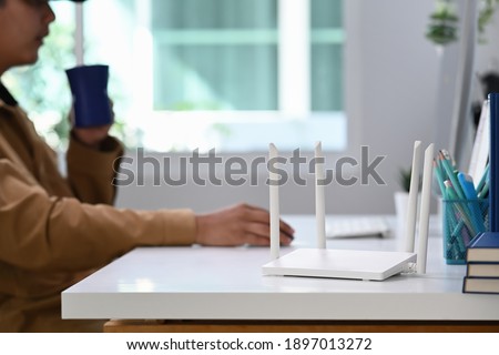 Closeup view of a wireless router with young man using laptop computer in background. Royalty-Free Stock Photo #1897013272