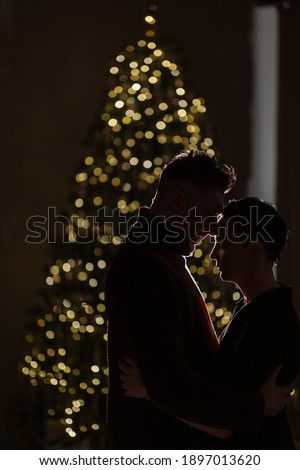 Silhouette of a lovely couple on the background of a Christmas tree and a fireplace. Christmas atmosphere and new year gift at home. Young family together.
