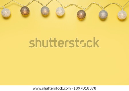 Gray white festive garland on yellow background flat lay top view. Cotton Balls Garland. Round bulbs LED festoon lights electric garland. Festive decoration Colors year 2021 Illuminating Ultimate gray