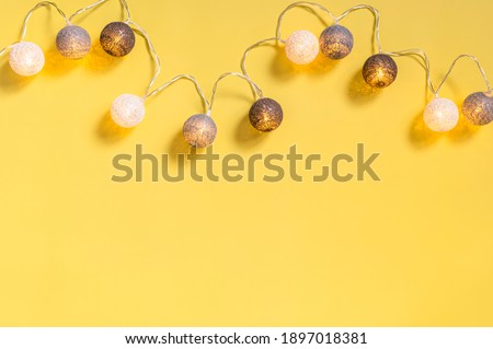Gray white festive garland on yellow background flat lay top view. Cotton Balls Garland. Round bulbs LED festoon lights electric garland. Festive decoration Colors year 2021 Illuminating Ultimate gray