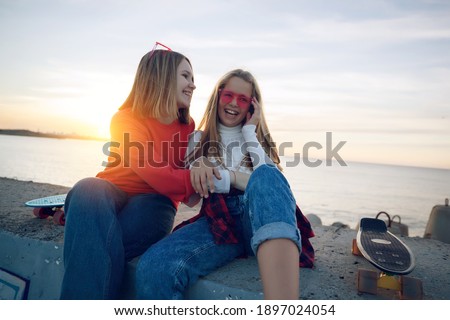 Two female friends playing with skateboard skateboard in the park. Girls with a skateboard. Laughter and fun. High quality photo.