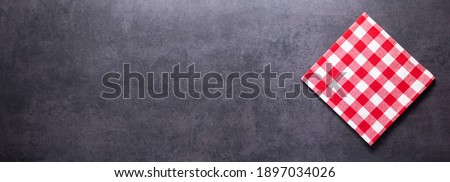 Folded checked or checkered tablecloth at stone surface of table. Top view as panorama of cloth napkin texture background with copy space