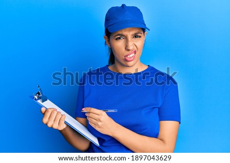 Beautiful brunette woman wearing courier uniform holding clipboard clueless and confused expression. doubt concept. 