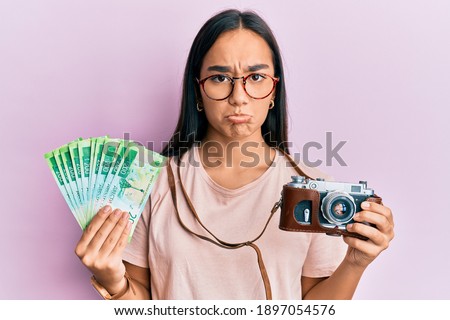 Young asian woman holding vintage camera and 200 russian ruble banknotes depressed and worry for distress, crying angry and afraid. sad expression. 
