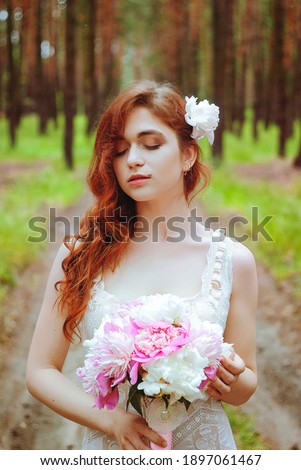 Outdoor portrait of young redhead woman in vintage wedding dress with big bouquet of pink peonies. Woman's Day. Female spring, summer fashion concept. Wedding day. The flowers delivery.