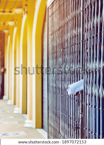White paper notification attached to closed retractable folding metallic gate.Metal collapsible sliding grille door normally use at shop houses in Asia. Bulletin sticking out at the gate of the house.