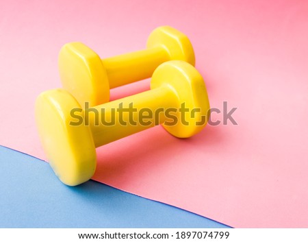 Yellow dumbbell color on pink, blue and yellow mat. Design of a sports poster or banner in fashionable colors of 2021
