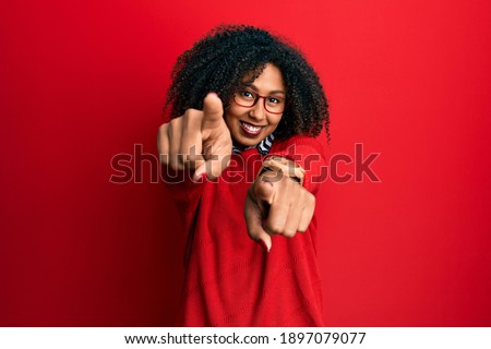 Beautiful african american woman with afro hair wearing sweater and glasses pointing to you and the camera with fingers, smiling positive and cheerful 
