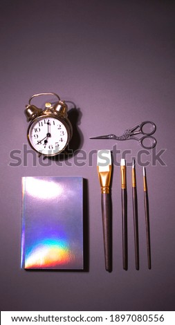 Golden alarm clock, brush set, scissors and holographic notepad on the vertical grey background with color inversion. There is a space for text.